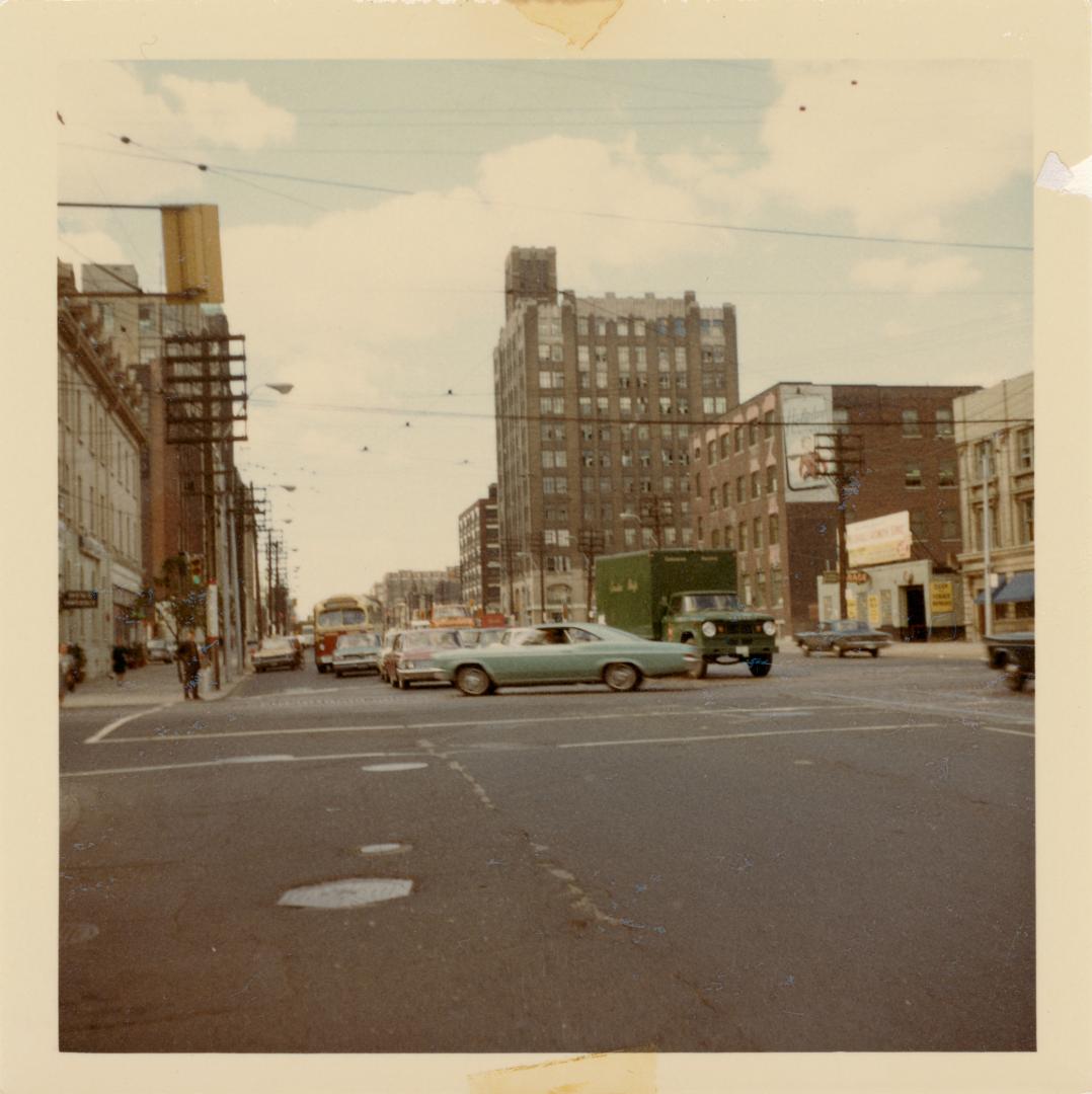 A photograph of a wide city intersection, with a public transit bus, cars and trucks parked and…