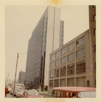 A photograph of row of warehouses and tall office buildings on the right side of a paved city s…