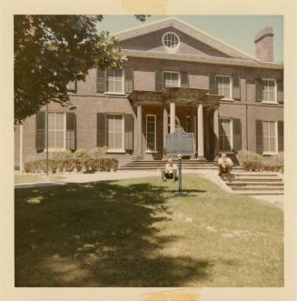 A photograph of a two story building with two sets of wide steps leading to an entrance flanked…