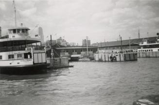 A photograph of a harbour, with docks and a ferry on the left side of the photo. The ferry has …