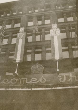 A photograph of a five story brick building decorated with bunting, a crown display and Royal c…