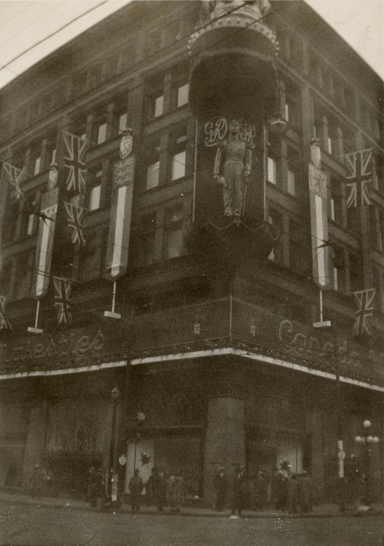 A photograph of a five story brick building decorated with bunting, a large crown sculpture and…