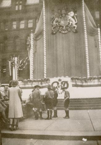 A photograph of a temporary stage and background standing in front of a large brick building. T…