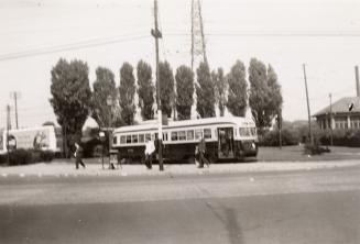 A photograph of a streetcar with its door open, parked to the left of a one story building and …