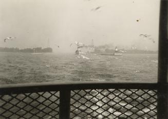 A photograph taken from the passenger area of a ferry, with a large body of water and other boa…