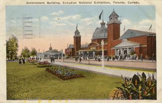 Colorized photograph of a large crowd of people standing on a road and lawn in front of a huge …