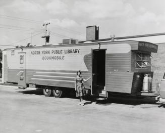 Woman holding door open on large bookmobile. 