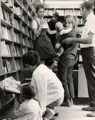 A group of people inside a bookmobile with a woman and child crouching looking at books and oth…