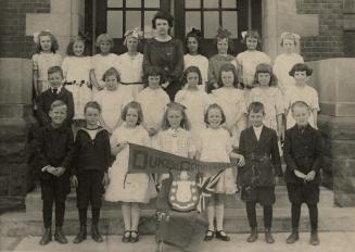 Picture of a school choir with children standing on the school steps holding banner and trophy.…