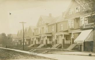 Black and white photograph of two-story houses lining a street.