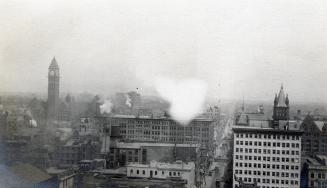 A photograph of a cityscape taken from a high vantage point. There are a number of multi-story …