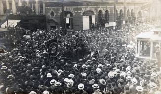 A photograph of a parade down a city street, with marchers and spectators completely filling th…