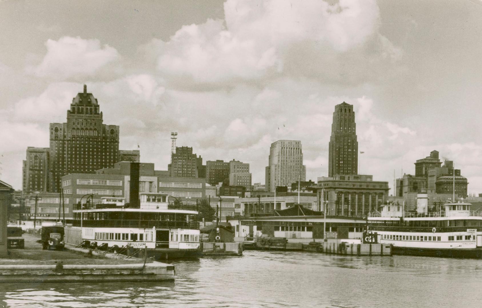 Black and white photo postcard depicting the Toronto harbourfront, dock, and ferries, with the …