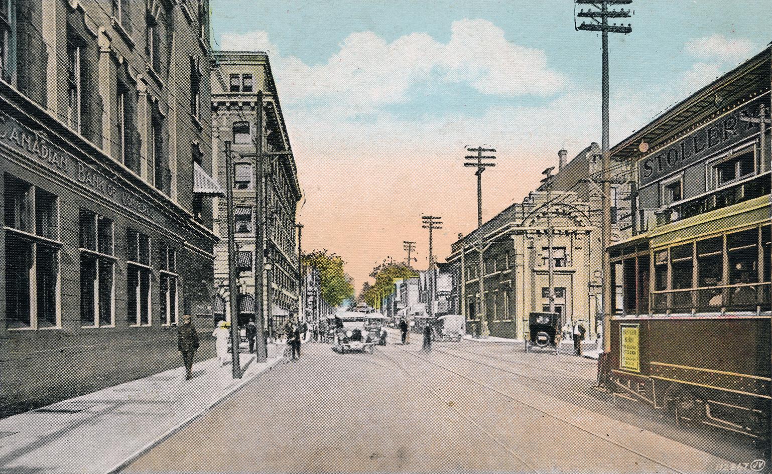 Colorized photograph of streetcars, automobiles and people traveling on a busy city street with…