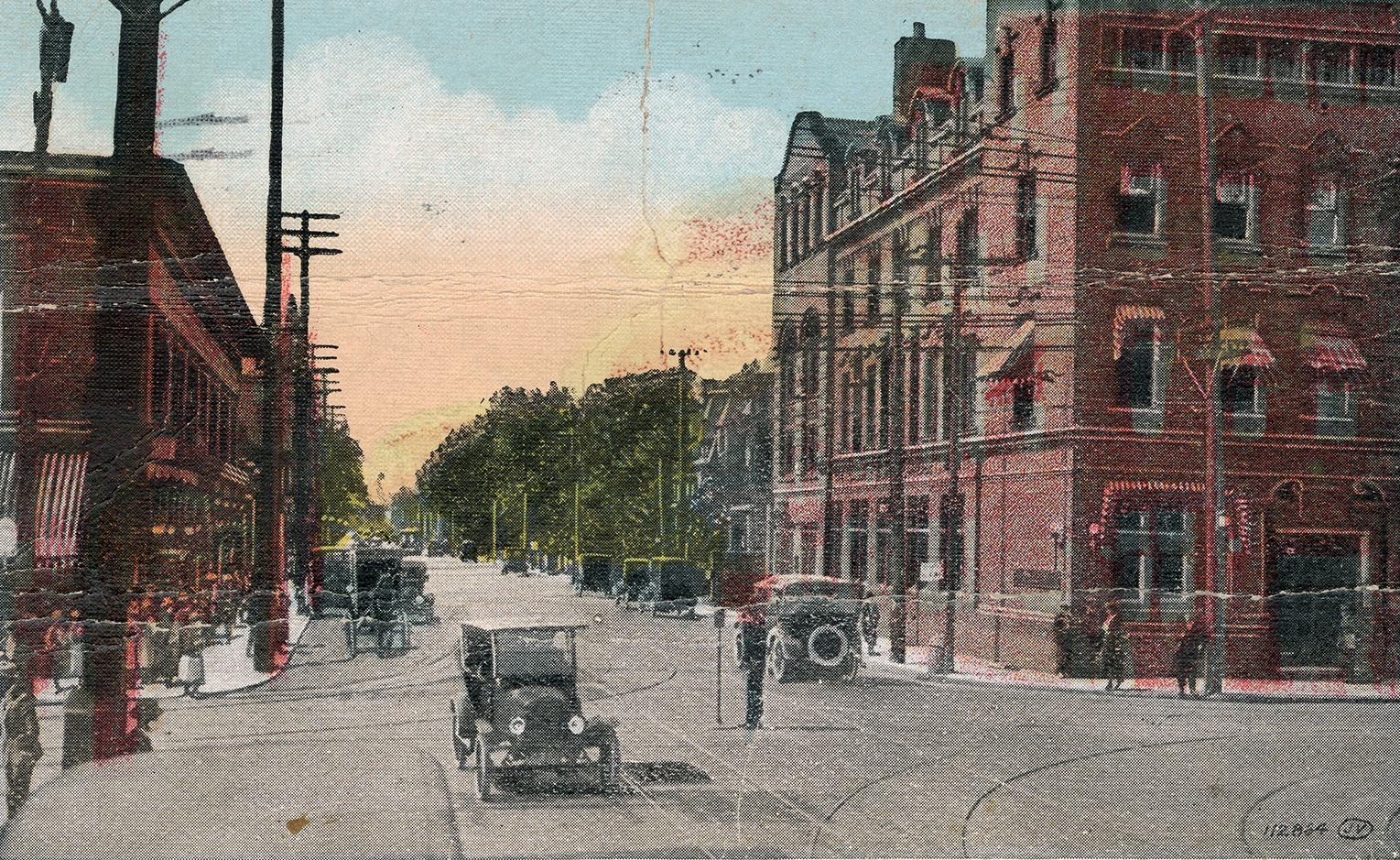 Colorized photograph of automobiles and people traveling on a busy city street with tall buildi…