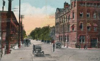 Colorized photograph of automobiles and people traveling on a busy city street with tall buildi…