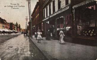 Colorized photograph of three ladies walking on the sidewalk outside of stores lining a downtow…