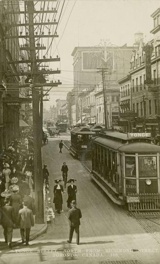 Black and white photograph of a very busy city street corner with automobiles and streetcars.