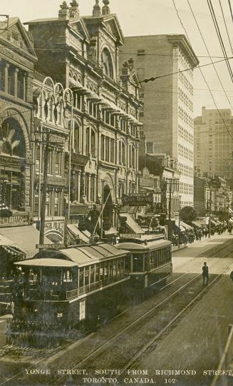 Black and white photograph of a very busy city street corner with automobiles and streetcars.