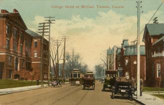 Colorized photograph of two automobiles and a streetcar on a street lines with large red brick …