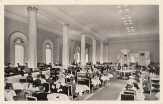 Black and white photograph of people eating at dining table is a large, formal dining room.