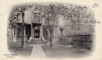 Black and white photograph of the front doorway of a three story building with bay windows.