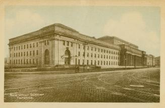 Colour photo postcard depicting Union station, bordered by cobblestone/brick-laid Front St. W. …