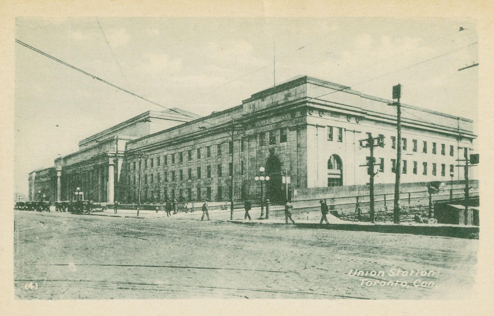 Green-toned photo postcard depicting Union station, bordered by an unpaved Front St. W. with pe…