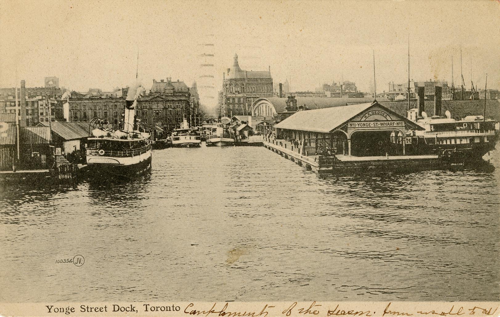 Black and white photograph of a steam boat moored in front of busy docks.