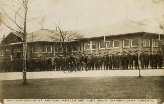 Black and white photograph of lines of servicemen in front of a one story building made of ceme…