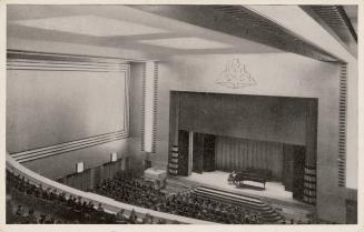 Black and white photograph of a person playing a piano on a stage in a theatre, taken from a lo…