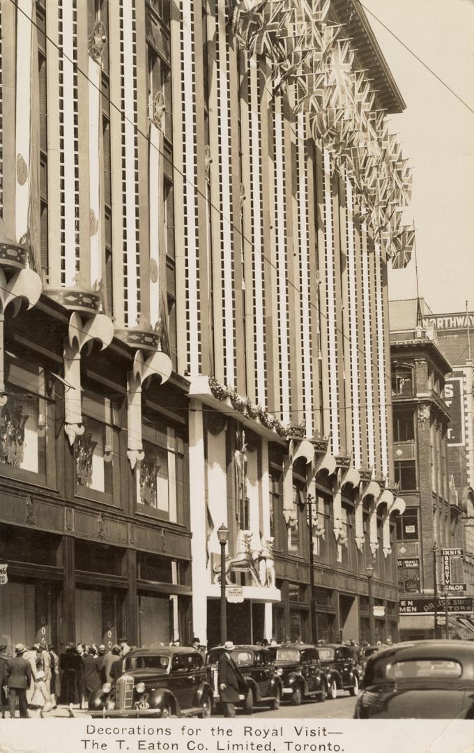 Black and white photograph of the front of a department store with banners and two lions rampan…