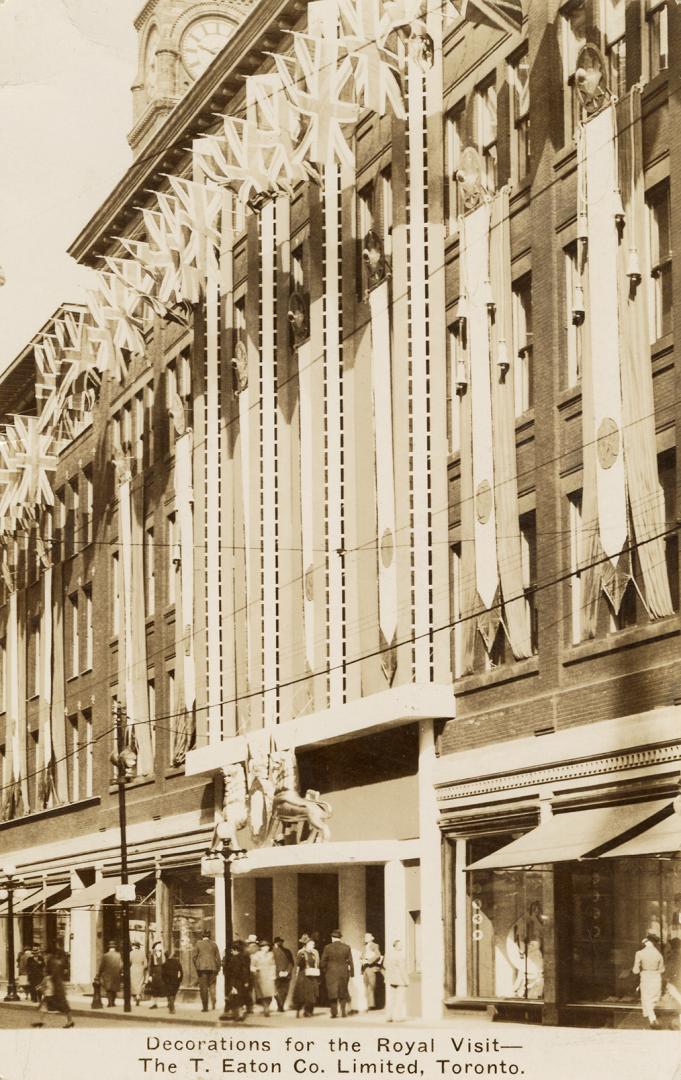 Black and white photograph of the front of a department store with a crest with the profiles of…