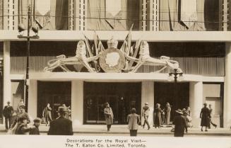 Black and white photograph of the entrance of a department store with a crest with the profiles…