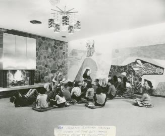 Picture of a librarian telling a story to a group of children in front of a fireplace with a la…