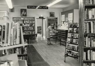 Picture of interior of library branch showing librarian at card catalogue and shelves of books.…