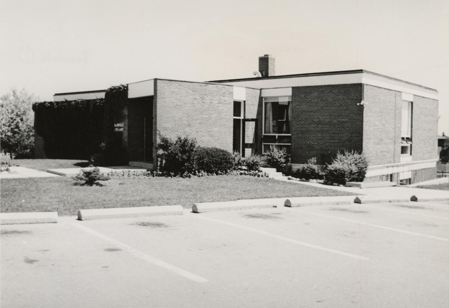 Picture of one storey library branch with empty parking lot in front. 