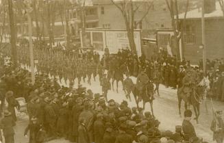 Black and white picture of soldiers marching on an icy city street while crowds of civilians lo…