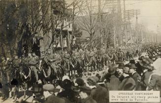 Black and white picture of soldiers on horses on a city street while crowds of civilians look o…