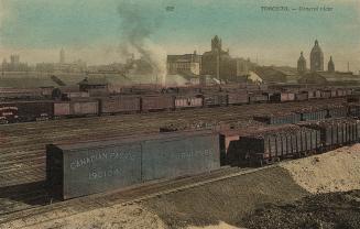 Colour photo postcard depicting a view of railroad cars sitting on many railroad tracks with th…