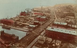 Colour photo postcard depicting an aerial view of buildings and the train track along the water…