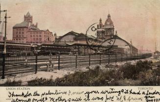 Colour photo postcard depicting a ground view of the tracks and exterior of Union station. The …