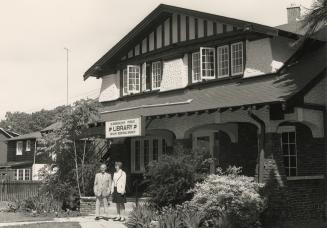 Picture of two people standing outside arts and craft style house used as a library. 