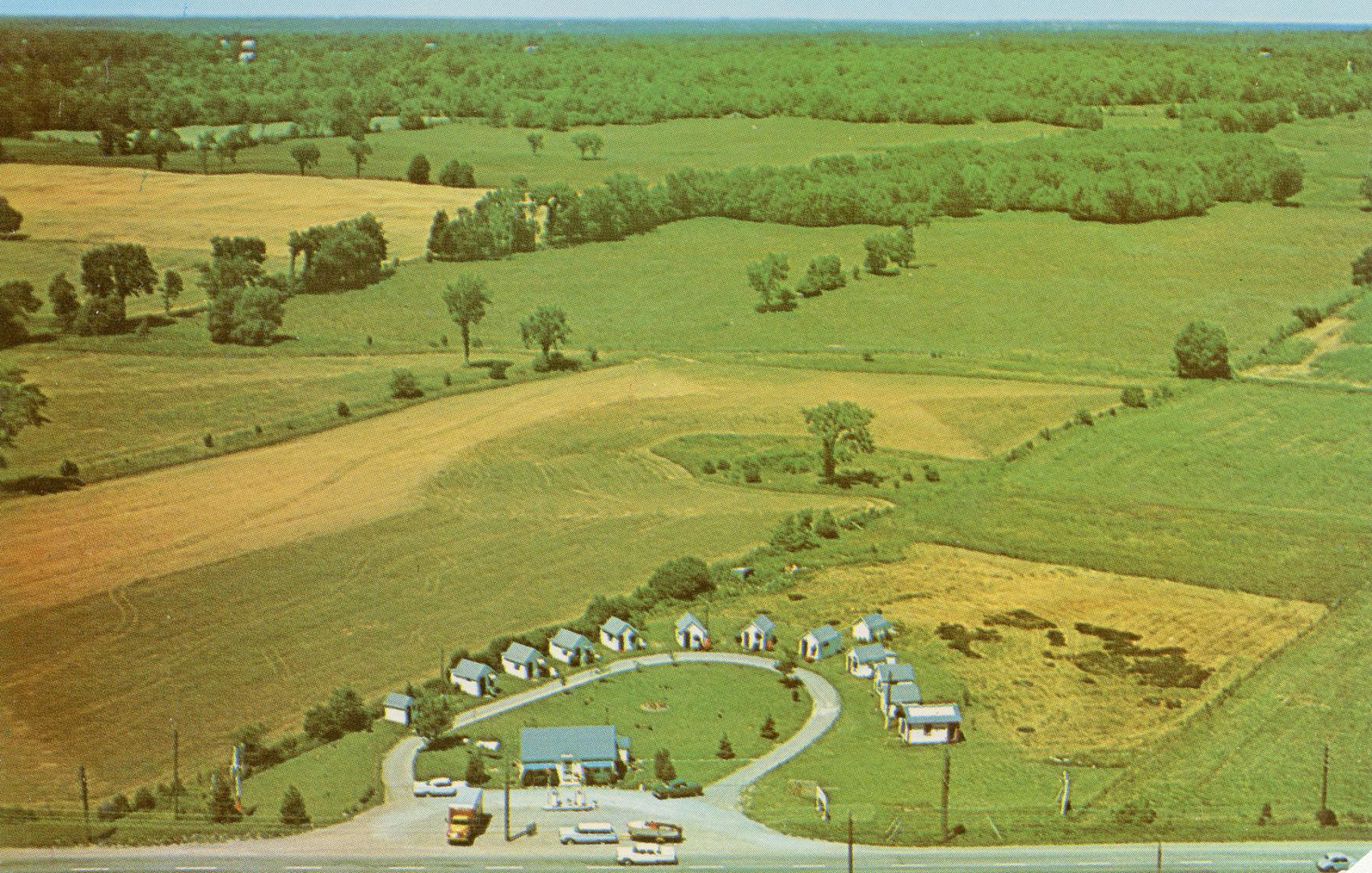 Color picture taken from the air of vacation cabins in a semi circle. Farmland is in the backgr…