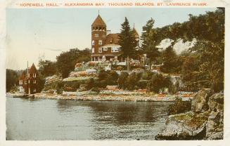 Colorized photograph of a view of a waterway, with a large summer resort on the river bank.