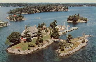 Colorized photograph of a view of a waterway, with a large home on an island connected by a sma…