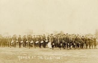 Black and white photograph of lines of servicemen in front of a one story building made of ceme…