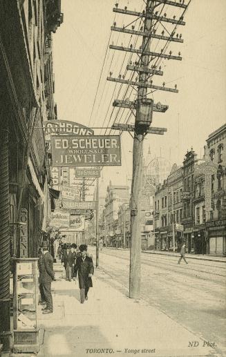 Sepia-toned postcard depicting a view of Yonge Street from the sidewalk with hydro poles and po…