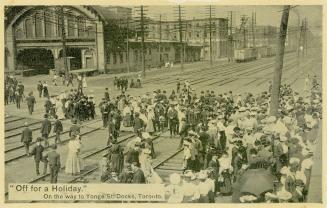 Black and white photo postcard depicting a crowd of people lined up to buy tickets for and cros…