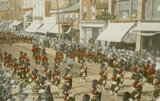 Colour postcard depicting a parade procession of men in red army attire and bearskin hats with …